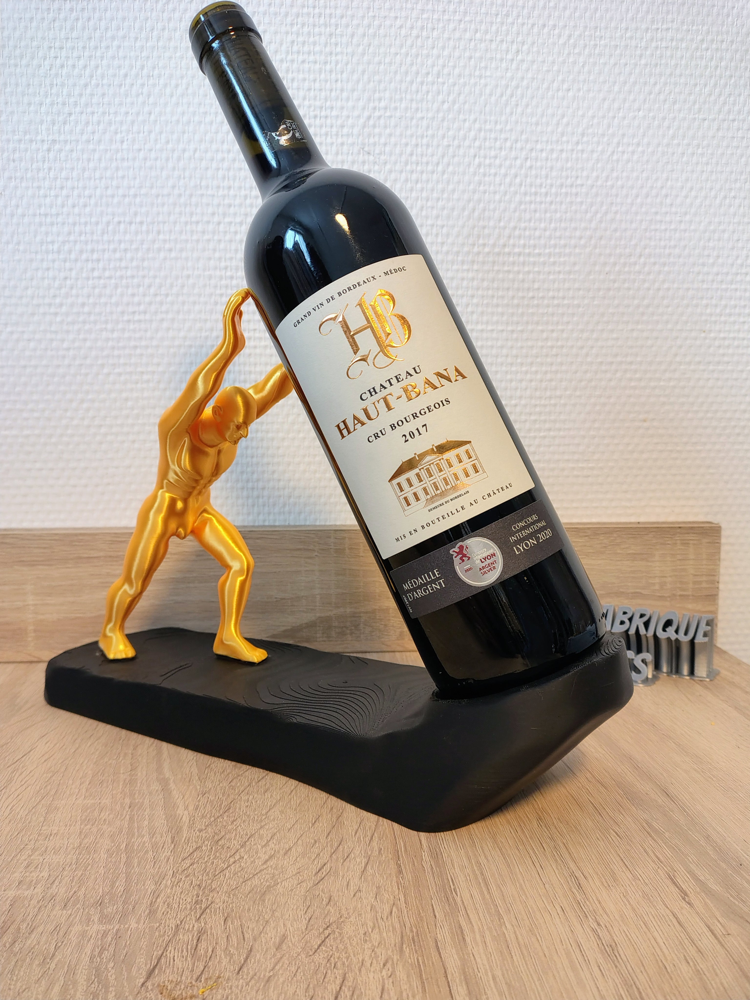 Support à vin design Hercule imprimé en 3D avec base noire texturée et figurine dorée pour bouteille de vin en équilibre.